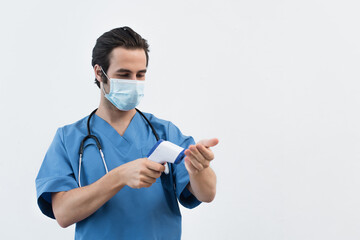 young doctor in medical mask measuring own temperature with pyrometer isolated on grey.