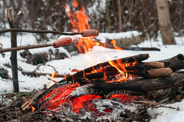 Sausages on the stick grilled in the fire. Winter forest.