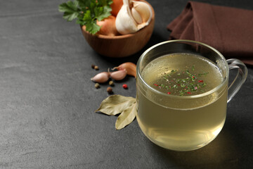 Hot delicious bouillon with dill in glass cup on black table. Space for text
