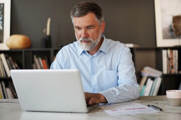 Portrait of senior man with grey hair working with laptop in office.