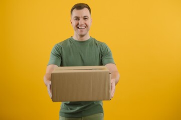 Delivery man in green uniform isolated on yellow background, studio portrait. Male employee working as courier dealer hold empty cardboard box. Service concept. Mock up copy space