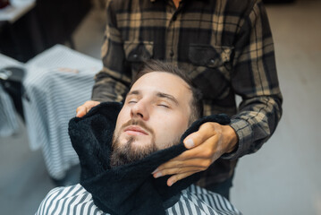 Barber preparing man face for shaving with hot towel in barber shop