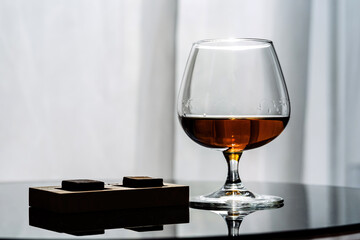 Natural cognac in a glass on a dark background on a black mirror surface, sweet sticks are falling.