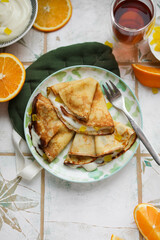 Orange pancakes with custard and candied fruits on a light plate. Pancake week, maslenitsa. Table setting in light style for lunch