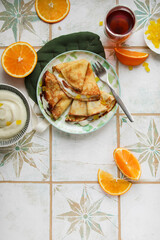 Orange pancakes with custard and candied fruits on a light plate. Pancake week, maslenitsa. Table setting in light style for lunch
