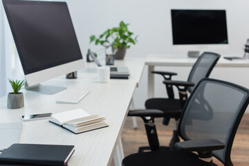 desks with computer monitors, blurred laptop and notebooks near office chairs.