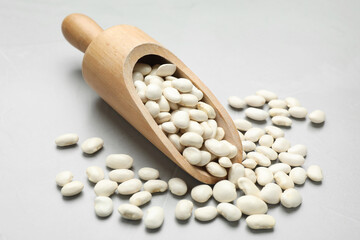 Wooden scoop with raw white beans on light grey table, closeup