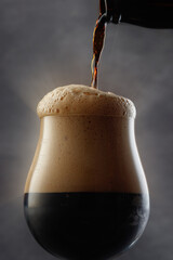 Detail of dark beer with overflowing foam head. Stream of dark stout pours into a beer glass....