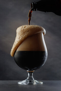 Stream of dark stout pours into a beer glass. Detail of dark beer with overflowing foam head. Selective focus	