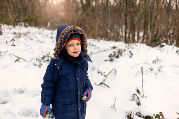 Photo of a little boy enjoys winter activities that snow brings. Portrait of a cute boy wearing a warm jacket with cap on a winter day. Happy little boy enjoying show. Cute toddler enjoying first snow