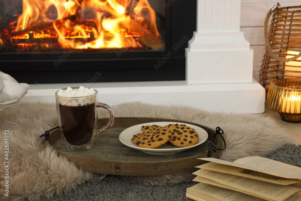 Poster Open book, hot drink and cookies near decorative fireplace in room. Cozy home atmosphere