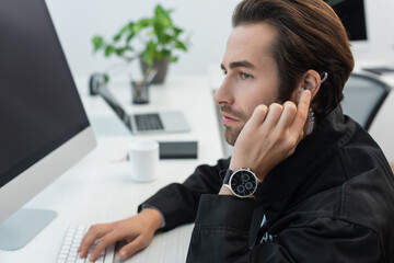 serious security man touching earphone while working in supervision room.