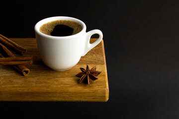 Coffee cup, anise and cinnamon on the wooden cutting board on the black background. Copy space. Close-up.