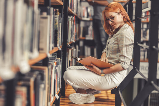 Red hair female student reading a book at the college library.	
