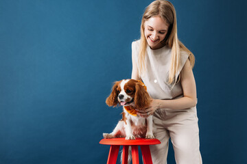 Pet owner standing in the studio. Little dog sitting on a red chair.
