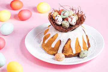 Easter cake with colorful eggs in a chocolate nest on pink background and flowers. Happy Easter concept. Dessert also known as  Kuglof. Top view