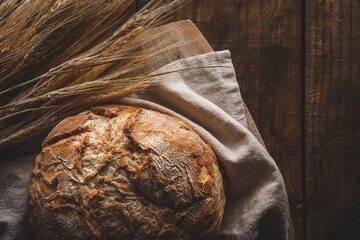 Vista superior de una hogaza de pan sobre una tela, con espigas de trigo, encima de una tabla de...