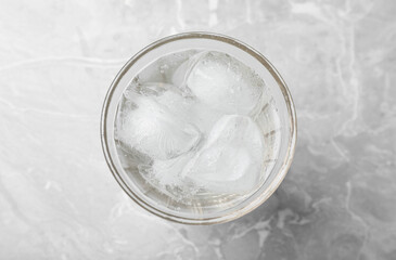 Glass of soda water with ice on grey table, top view