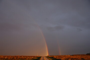 Amber sunset with double rainbow over ridge land.