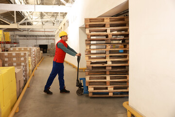 Fototapeta premium Worker moving wooden pallets with manual forklift in warehouse