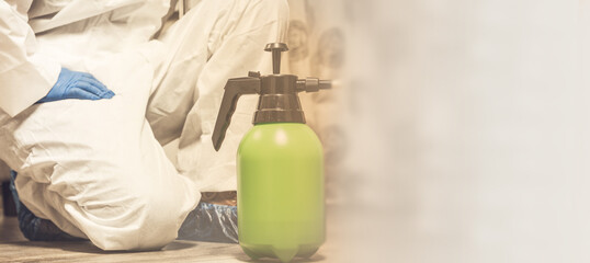 Spray bottle with pesticides close-up. An exterminator in work clothes sprays pesticides from a spray bottle. Fight against insects in apartments and houses. Disinsection of premises