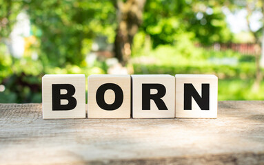 Four wooden blocks lie on a wooden table against the backdrop of a summer garden and create the word BORN.