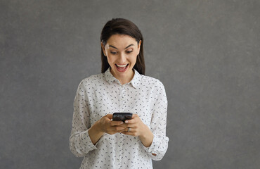 Pleasantly surprised woman holding a phone in her hands reads positive comments in publications on...