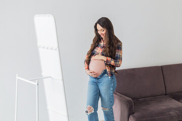 pregnant woman looking at herself in the mirror. Young pregnant woman in the room