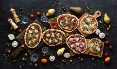 Several pizzas on cutboards with ingredients: pears, tomatoes, mushrooms