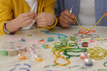 Father with his daughter making beaded jewelry at table, closeup