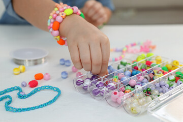 Little girl making beaded jewelry at table, closeup - obrazy, fototapety, plakaty