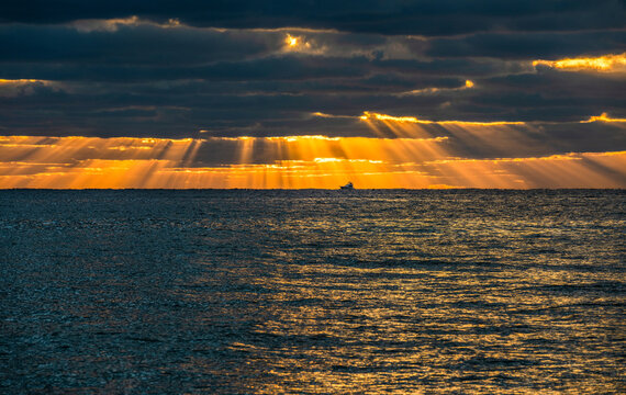 Sunrays&nbsp;and golden clouds over ocean at sunrise with small fishing boat in distance