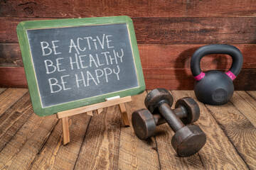 Be active, be healthy, be happy   inspirational concept -  white chalk text on a slate blackboard sign against weathered rustic wood with a dumbbells and kettlebell