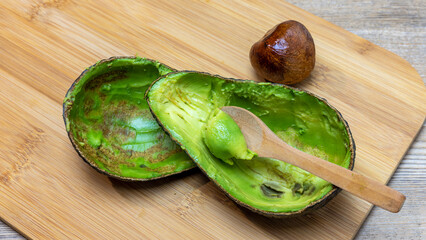 avocado cut and emptied of pulp with wooden spoon on bamboo cutting board, panorama vegan food, gluten free