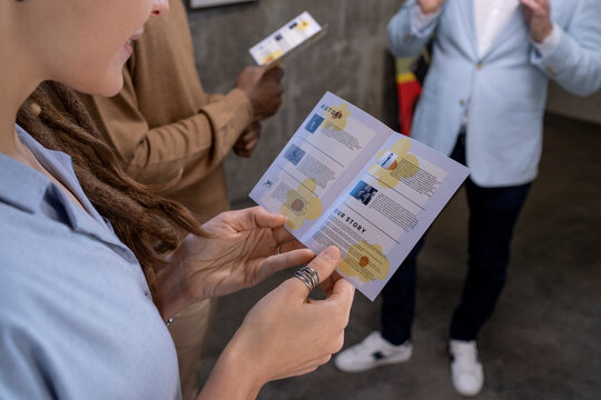 Close-up of young woman examining the guide about the artwork with other people during excursion in art gallery