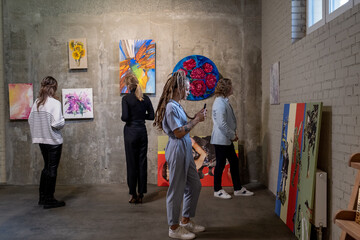 Woman photographing the picture on mobile phone, she visiting exhibition in art gallery with other...