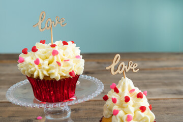 Valentine's Day. Two cupcakes with red topping decoration and wooden sign with the word LOVE on a wooden background.
