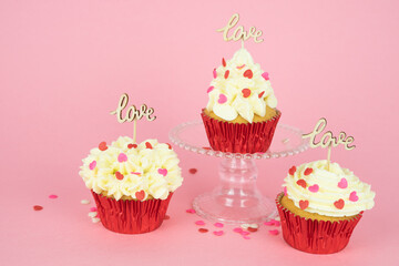 Valentine's Day. Three cupcakes decorated with red topping and a wooden sign with the word LOVE on a pink background. Copy space.