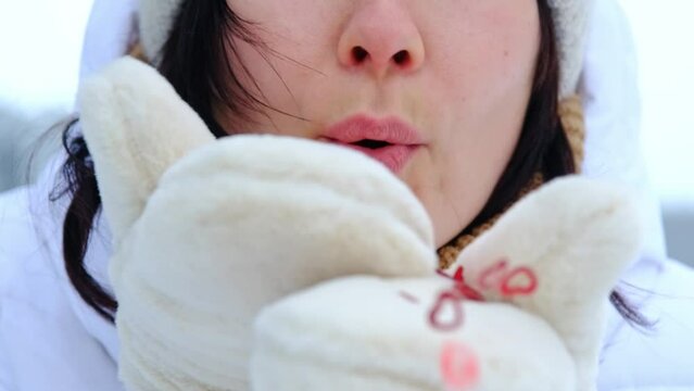A woman blows red sequins in the shape of hearts from warm fur mittens. Slow-motion video, close-up. Valentine's Day, love, feelings