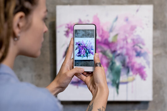 Close-up of young woman making photo of beautiful painted picture on the wall on her mobile phone