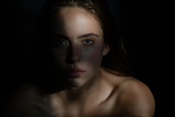 Girl face in shadow. Young woman posing at studio over black background. Light and shadow. Fashion portrait of beautiful woman with dark light on face.