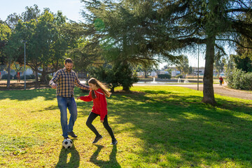 Happy father and cute smiling daughter playing soccer together at park.
