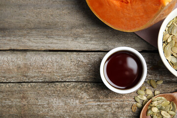 Bowl of oil and pumpkin seeds on wooden table, flat lay. Space for text