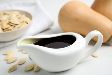 Gravy boat of pumpkin oil and seeds on white table, closeup