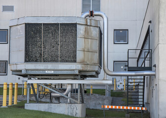 Large industrial air filtration unit mounted on concrete pads outside of stucco building, daytime,...