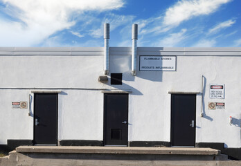 Fototapeta na wymiar Exterior facade of a blast-proof flammable stores facility, white stucco, black steel doors, exhaust chimmneys, sunny day, clouds, nobody 