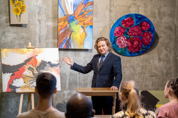 Mature painter in suit presenting his paintings to the people during his presentation in art gallery