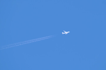 Distant passenger jet plane flying on high altitude on clear blue sky leaving white smoke trace of contrail behind. Air transportation concept
