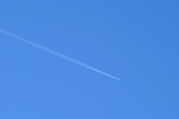 Distant passenger jet plane flying on high altitude on clear blue sky leaving white smoke trace of contrail behind. Air transportation concept