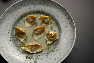 Fresh wonton dumplings with meat are presented on a round gray plate close up. Restaurant serving...